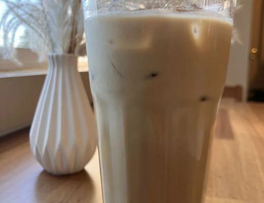 An iced latte in a fluted glass on a wooden table beside a vase of pampas grass